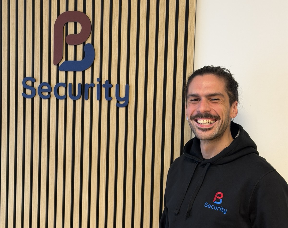 Jonathan standing beside the PB Security sign in the office, wearing a PB Security hoodie