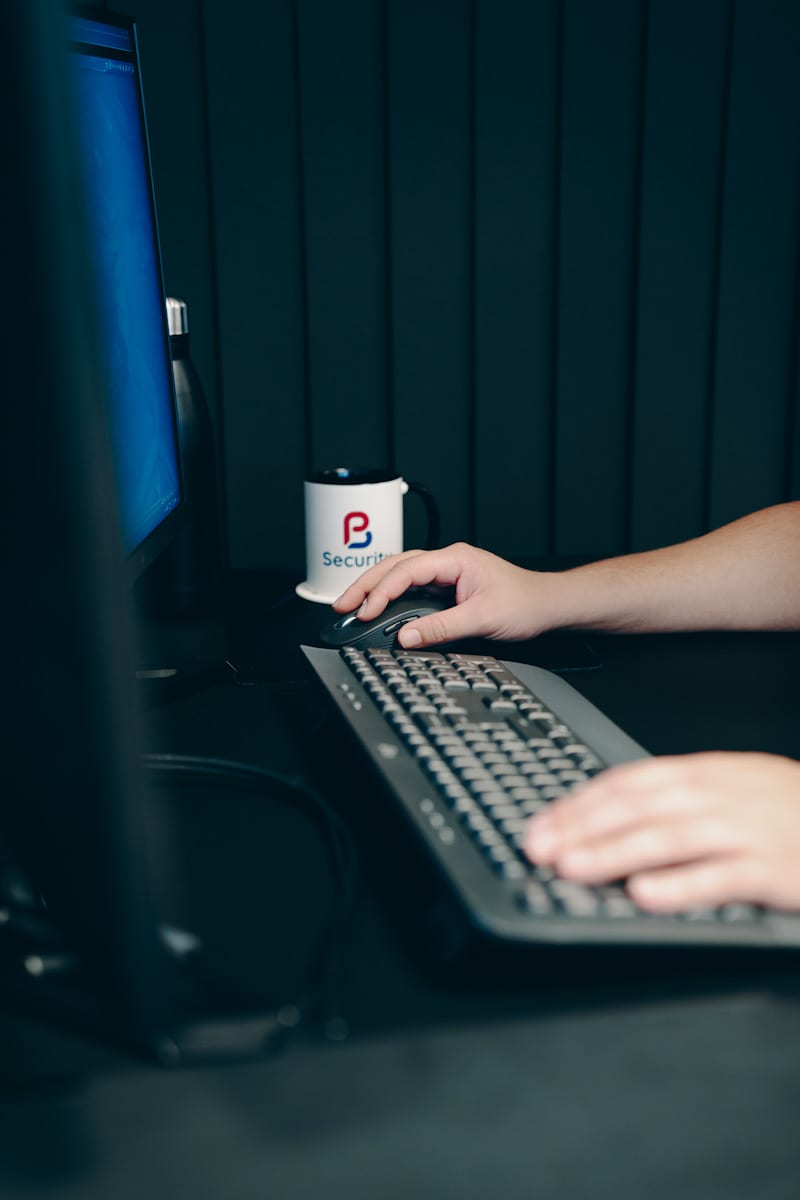 A hand on a keyboard at a PB Security workstation, with a PB Security mug beside the screen